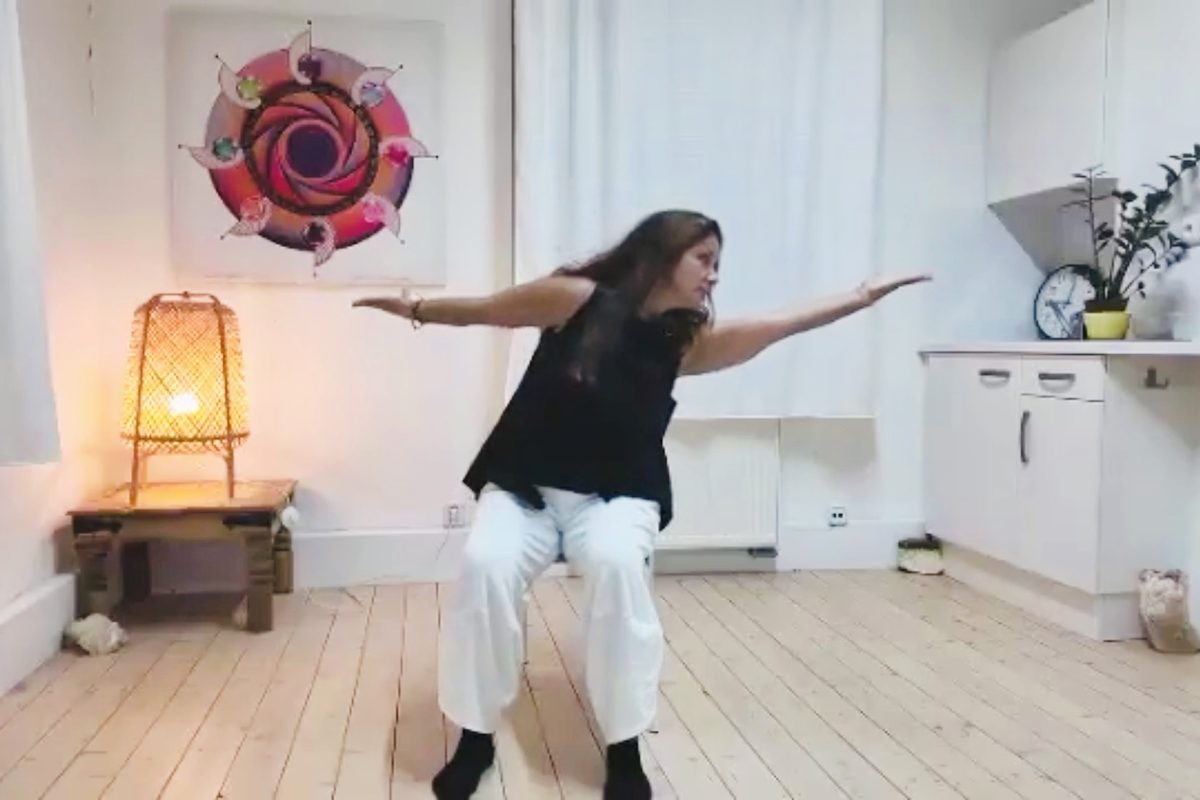 Michaela Liyah Sklářová cvičí čchi-kung na židli s rozpaženýma rukama ve světlé místnosti